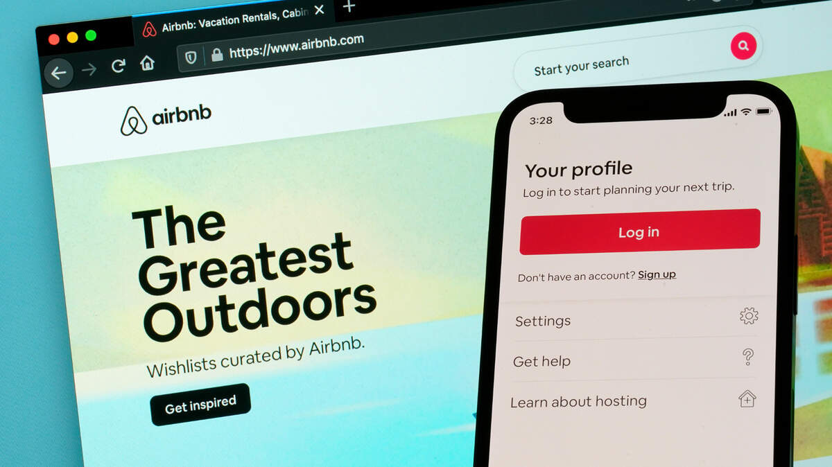 The login page for Airbnb’s iPhone app is seen in front of a computer displaying Airbnb’s website. Airbnb says it’s taking steps to prevent people from throwing parties at houses they rent for the Memorial Day and July 4 holidays. Airbnb said that it will bring back restrictions that it says worked last summer. Many customers will be barred from making one-night reservations for houses, and there will also be limits on who can make two-night bookings.