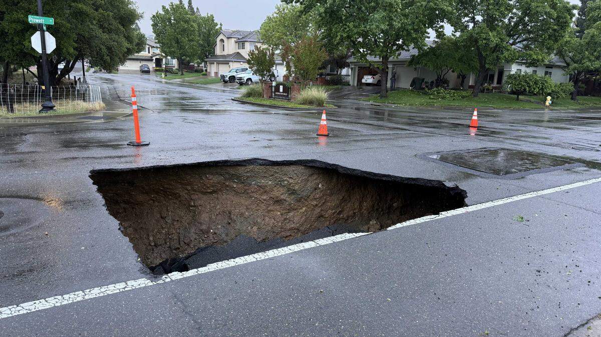 A large sinkhole blocks the intersection of Prewett and Newington drives in the Lexington Hills neighborhood of Folsom on Monday, April 13, 2026. The sinkhole opened after a series of weekend storms brought heavy rain to Northern California, prompting crews to install barriers and set up detours for residents.