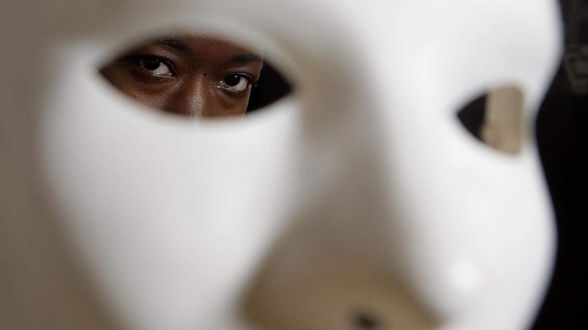 Massachusetts Institute of Technology facial recognition researcher Joy Buolamwini stands for a portrait behind a mask at the school, in Cambridge, Mass., in 2013. Buolamwini’s research has uncovered racial and gender bias in facial analysis tools sold by companies such as Amazon that have a hard time recognizing certain faces, especially darker-skinned women. Buolamwini holds a white mask she had to use so that software could detect her face..