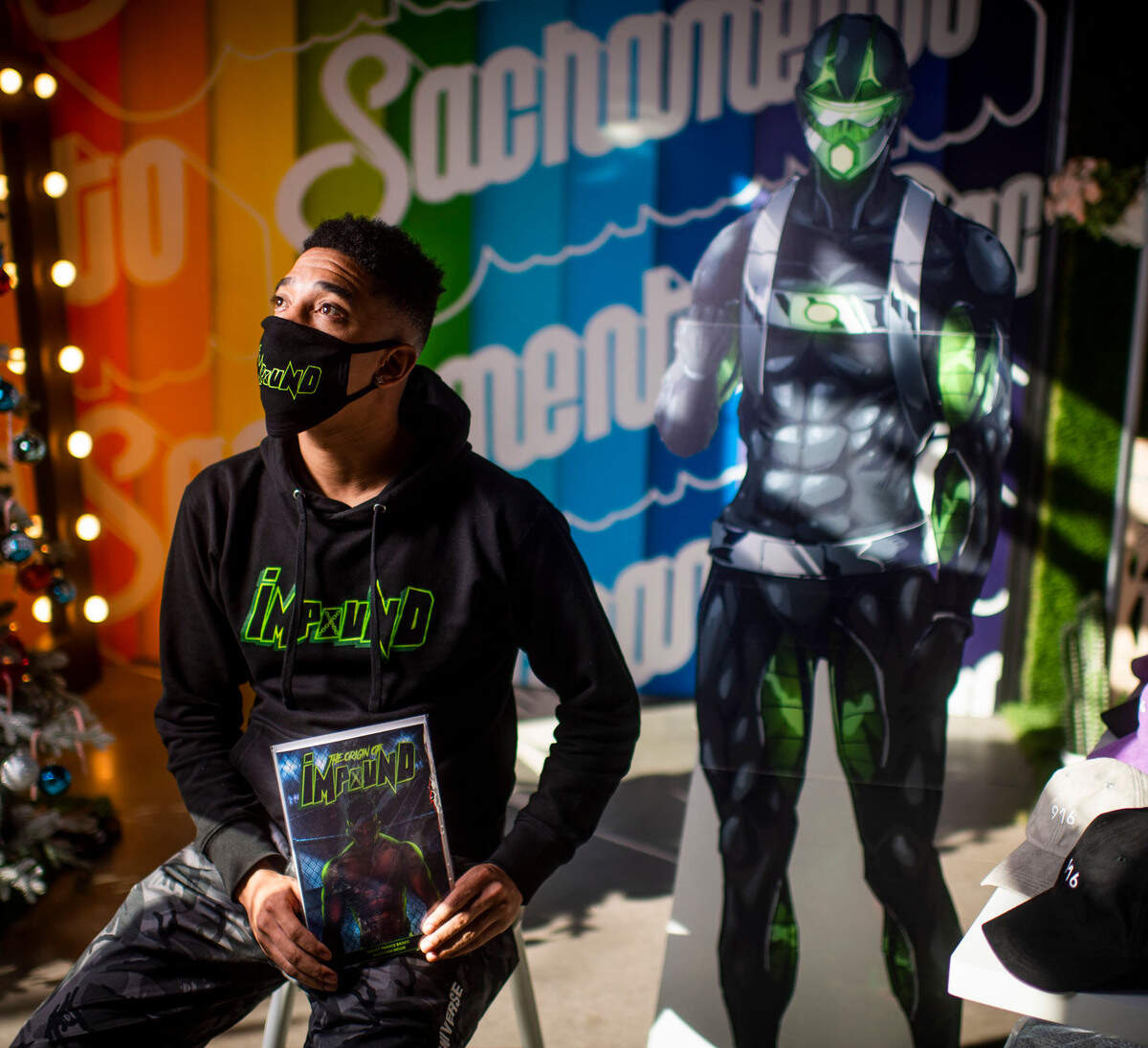 Impound Comics creator Brent Trayce Sands holds one of his comic books at the People of Sacramento store in the Ice Blocks on Tuesday, Dec. 29, 2020. Behind him stands a cutout of his superhero character Impound, a Black single father who is also an MAA fighter.