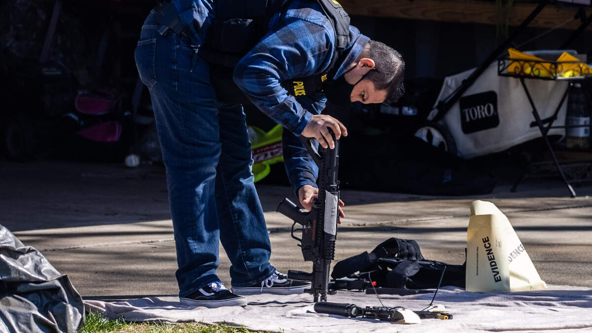 A police officer examines a rifle, part of an enormous trove of guns and explosives, in the driveway of a home on Mission Avenue in Carmichael on Thursday, Feb. 25, 2021.