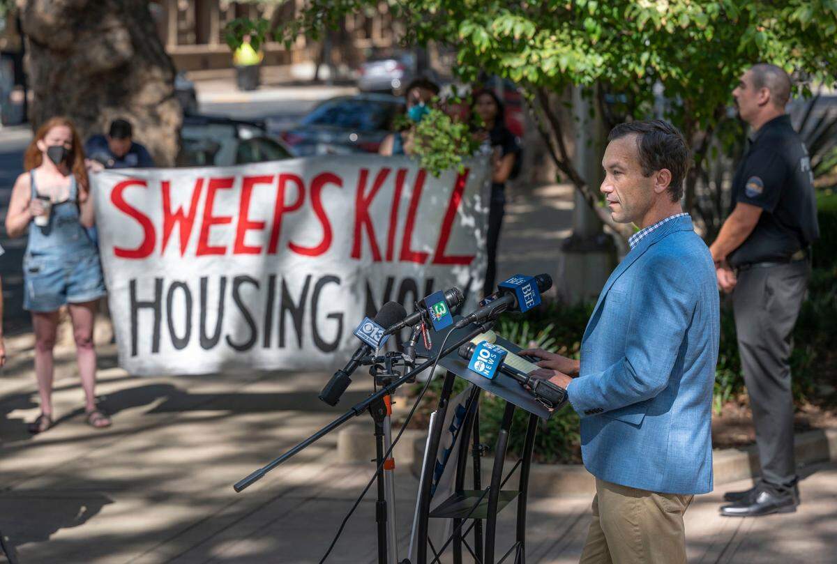 Daniel Conway, a lead proponent of Measure O, the Sacramento homeless shelter ballot measure, talks at a press conference in Sacramento on Aug. 4 as a group of homeless activists protest the event holding a sign that says “Sweeps Kill. Housing Now.”