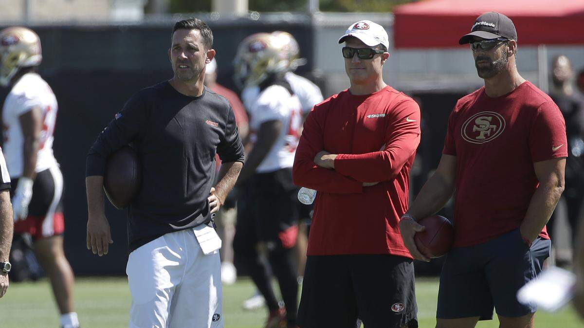 Coach Kyle Shanahan, left, general manager John Lynch, center, and broadcaster Tim Ryan watch over a recent 49ers training camp practice in Santa Clara.