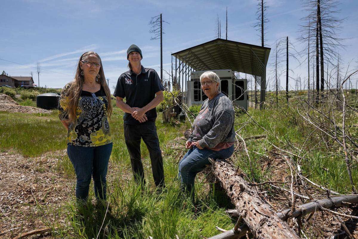 Jenny Magidson, 67, Tobe Magidson, 49, and Penny Singleton, 68, on May 1 stand outside the trailer where Jenny Magidson has lived since the 2021 Caldor Fire. Tobe Magidson bought the property after the fire destroyed his home in another part of Grizzly Flats and plans to build his new home next to trees that survived the fire.