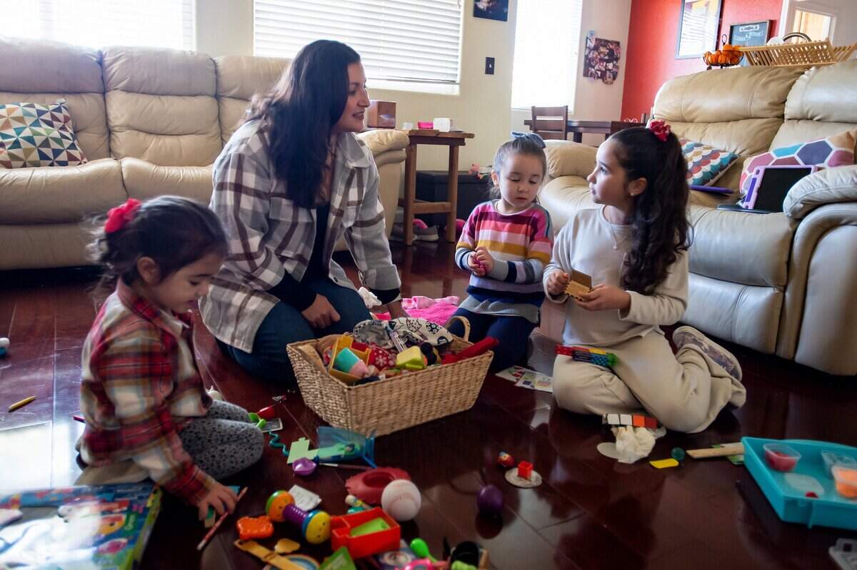 Augustina Kuen helps her children Amelia, left, 3; Olivia, second to right, 4; and Norah, right, 9; clean up their toys in the living room on Sunday, Jan. 22, 2023, at their home in Elk Grove. The three girls haven’t seen their father Aaron in person since he went into cardiac arrest during the marathon, Augustina said, due to hospital and facility regulations.