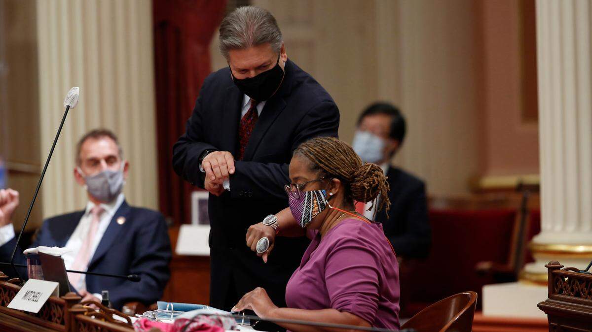 Sen. Holly Mitchell, D-Los Angeles, chair of the Senate Budget and Fiscal Review Committee, gets an elbow bump from Sen. Robert Hertzberg, D-Los Angeles, after the Senate approved the $202.1 billion state budget at the Capitol in Sacramento on Thursday, June 25, 2020. Mitchell carried the bills that made up the spending plan that covers the state’s estimated $54.3 billion deficit brought on by the coronavirus. The Assembly is scheduled to vote on the budget Friday.