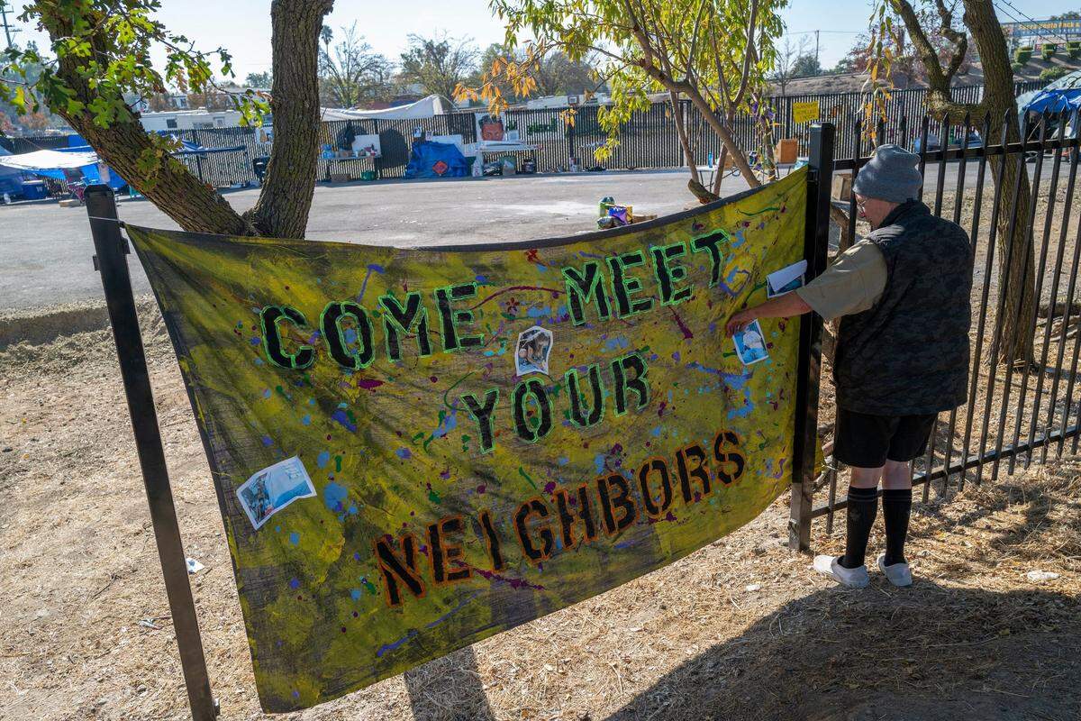 Sharon Jones, who is homeless and living at an encampment she named “Camp Resolution,” placed a sign with pictures of homeless residents to welcome cyclists along the bike trail near Arden Way and Colfax street in Sacramento on Wednesday. The camp was closed since April but earlier this month advocates from Oakland came and assisted homeless residents from Sacramento to reclaim it after the city did not make it a safe parking lot or build tiny homes as promised, said Jones.