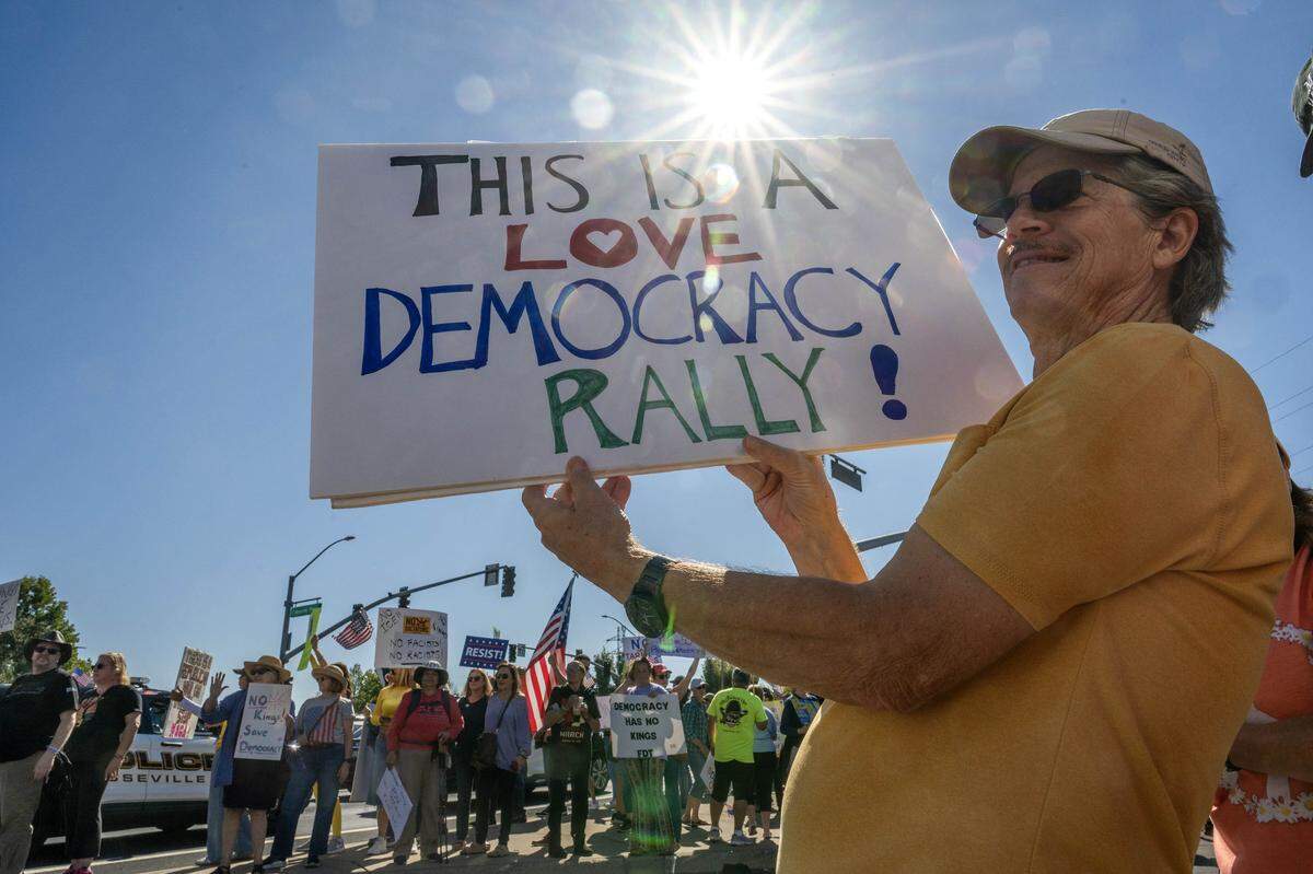 Don Fallon, of Lincoln, holds a sign that says "This is a love democracy rally" as he participates in a “No Kings” rally in Roseville on Saturday, Oct. 18, 2025.
