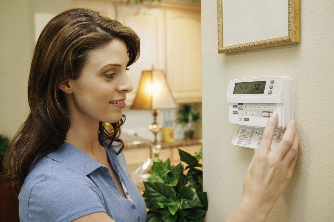 A woman adjusting a thermostat at home.