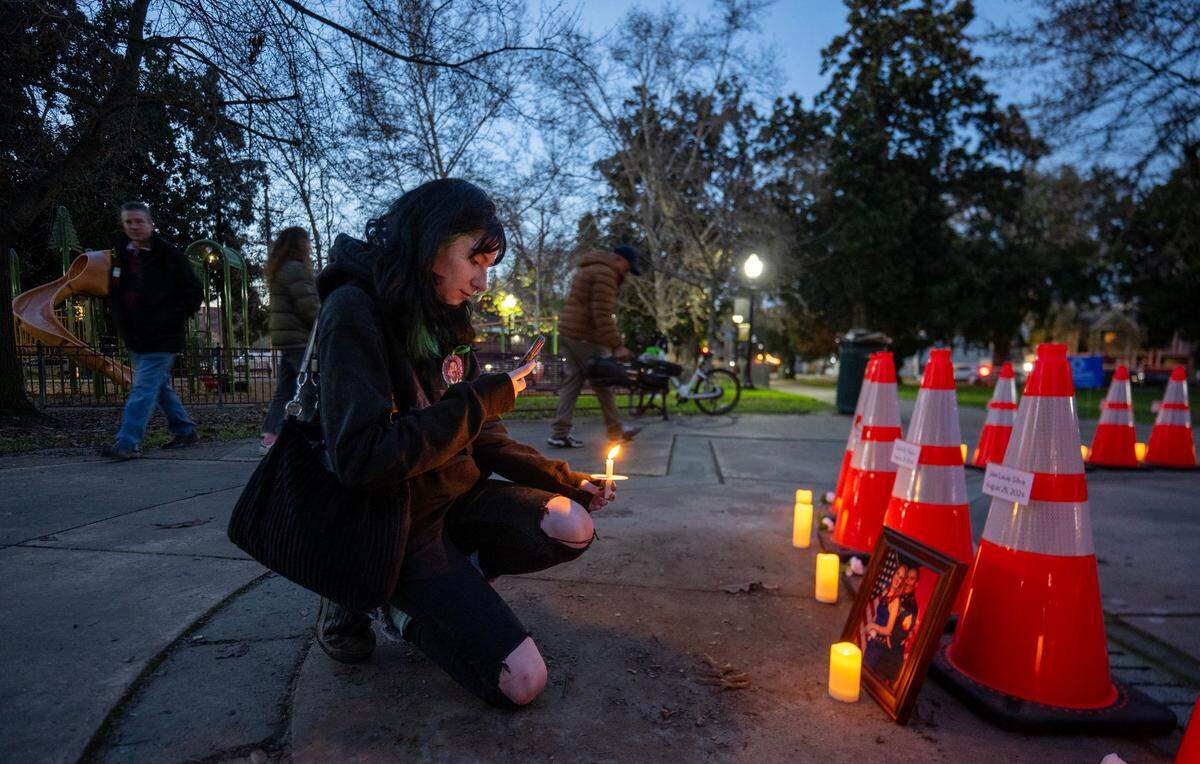 During a vigil hosted by Slow Down Sacramento for people killed in city traffic collisions, Lunden Almquist takes a picture of a framed photograph in front of a cone on Thursday. The photograph shows her late stepfather, José Luis Silva, who was killed in 2024 while riding his motorcycle in midtown with Almquist’s mother, Michelle Silva.