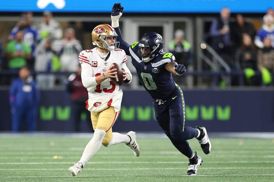 Quarterback Brock Purdy of the San Francisco 49ers is pressured by DeMarcus Lawrence of the Seattle Seahawks during the second quarter in an NFC divisional round playoff game at Lumen Field on Saturday in Seattle.
