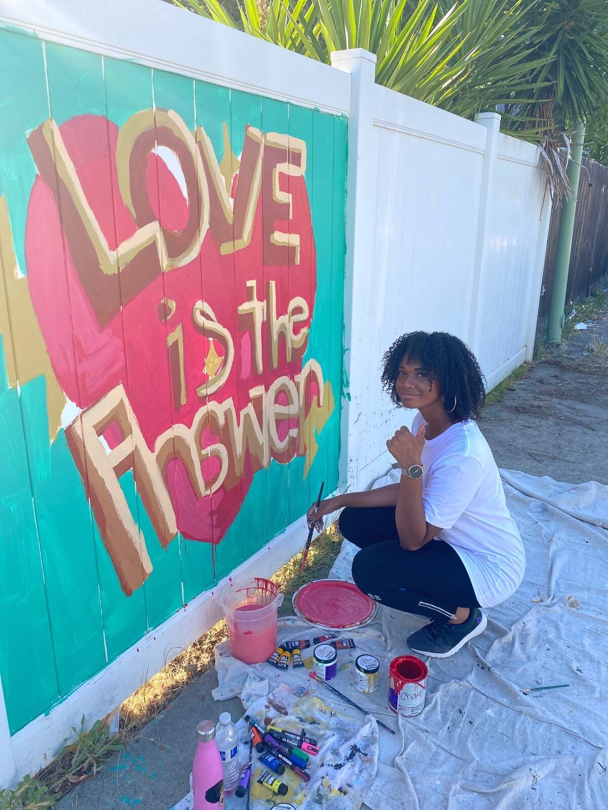Desaree Decker sits in front of a mural, “Love is the answer,” that she painted for the Imagine a New World project.