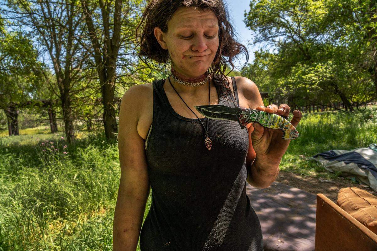 Christina Qualls holds the “pocket knife” she uses to protect herself in April at her encampment along the American River bike trail, near where the body of homeless woman Kathy Lynn Robbins in a suspected homicide. “It’s difficult out here for being a woman, like some people have been raped like me,” she said. Qualls said they also carry guns. “They carry them for protection from the bad things that have happened to them.”