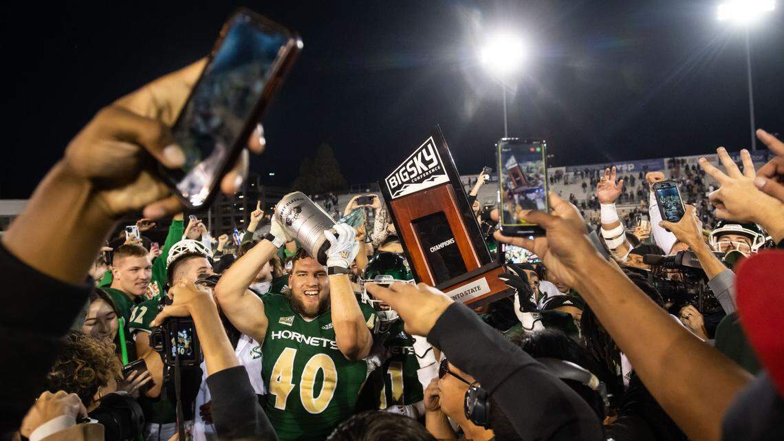 Sacramento State Hornets defensive lineman Killian Rosko (40), left, raises the Causeway Classic prize alongside a conference trophy while players, students and fans rush the field after their win over UC Davis at the NCAA college football game Saturday, Nov. 19, 2022, at Hornet Stadium in Sacramento.