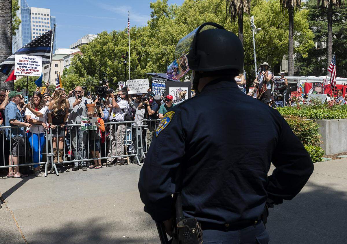 Pastor Tim Thompson of Riverside holds an olive tree and offers it to the law enforcement officers during a protest at the state Capitol on Thursday, May 7, 2020 in Sacramento during the coronavirus pandemic.
