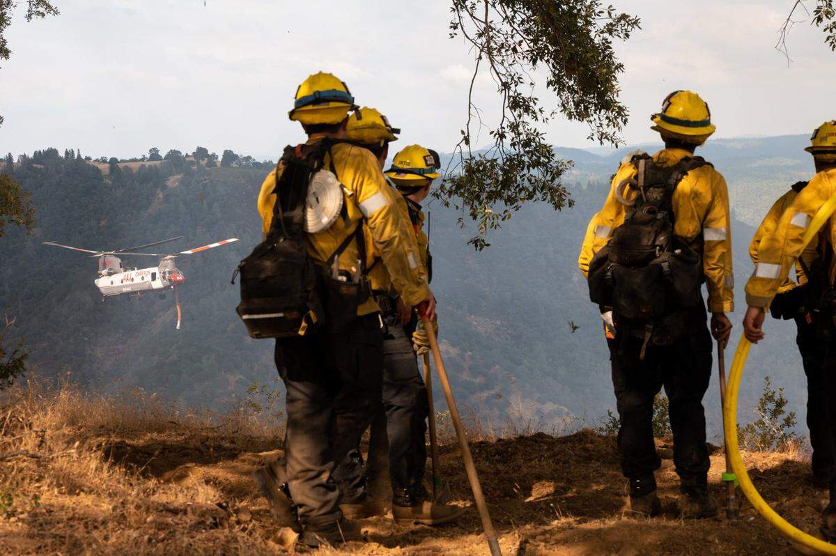 A Billings CH-47 Chinook fire fighting helicopter flies by a Cal Fire crew before dropping water on the Electra Fire near Pine Grove in Amador County on Tuesday, July 5, 2022. The fire had burned over 3,000 acres and there are mandatory evacuations in Amador and Calaveras counties.
