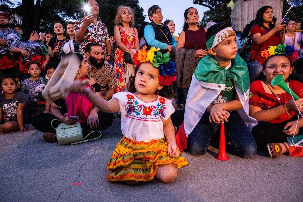 Abigail Story Perez, 3, plays with a matraca, a wooden spinning rattle, as she and her brother Axel Liam Perez, 8, second from right, celebrate the Mexican Day of Independence at the state Capitol on Thursday, Sept. 15, 2022.