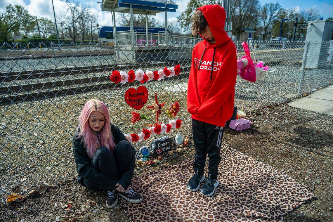 Ryley French, 10, gazes down at his mother, Erika Pringle, 37, as she closes her eyes in meditation, wearing a favorite hoodie that belonged to her late brother, Andrew Pringle, whose memorial she created on March 18 in Rosemont. Erika has visited the site twice a week for the past two years since her brother was struck by a motorist in 2023 while crossing Folsom Boulevard to get McDonald’s lunch before catching the light rail to work — he later died at the hospital.
