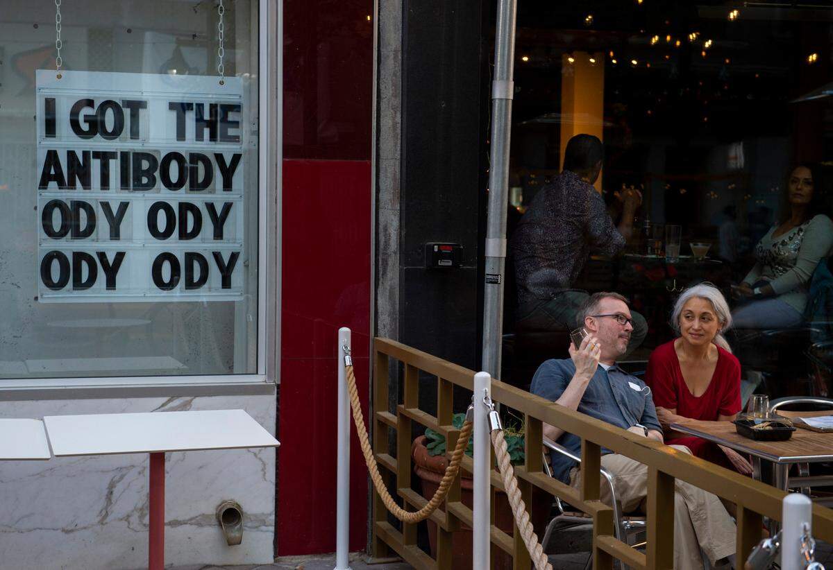 Patrons sit outside MidiCi Neapolitan Pizza on K Street in downtown Sacramento next to a sign in the window of Solomon’s Deli on Saturday, June 5, 2021.
