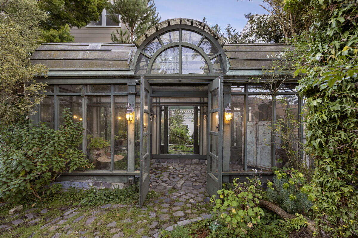 A traditional, grand, glass-paned greenhouse/conservatory anchors the garden in storybook fashion.
