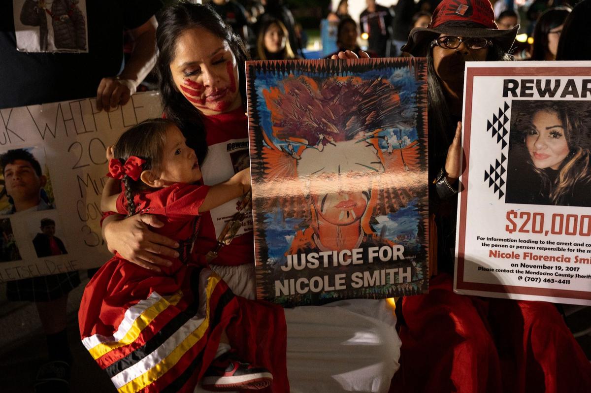 Bernadette Smith sits with a red handprint painted across her face with her daughter Chishkaleh Flores, 2, at the Missing and Murdered Indigenous People vigil at the Capitol on May 1. She holds a sign of her sister, Nicole Smith, who was murdered in 2017 on the Manchester Rancheria. Her murder is now a cold case.