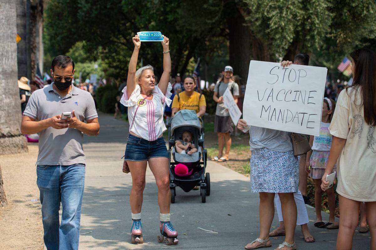 Holly Baade, a Democrat who is running in the Sept. 14 recall election, holds up her bumper sticker while skating through a rally against requiring vaccines for health care workers at the state Capitol on Monday, Aug. 16, 2021. A couple hundred people gathered to speak out on the mandatory vaccination.