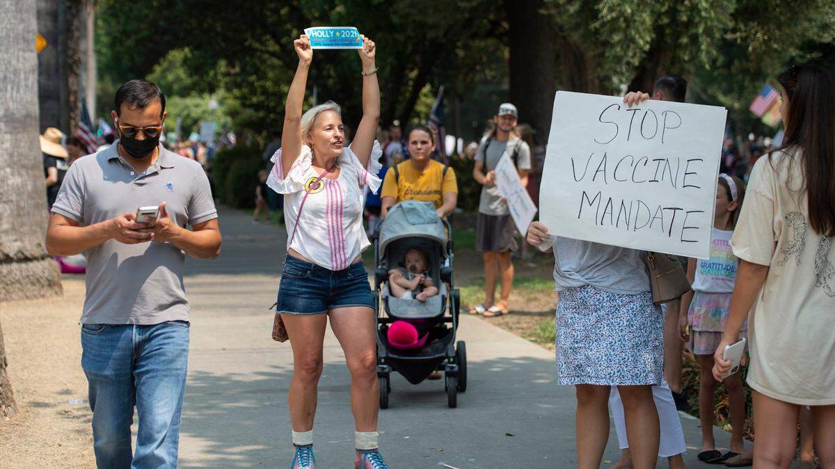 Holly Baade, a Democrat who is running in the Sept. 14 recall election, holds up her bumper sticker while skating through a rally against requiring vaccines for health care workers at the state Capitol on Monday, Aug. 16, 2021. A couple hundred people gathered to speak out on the mandatory vaccination.