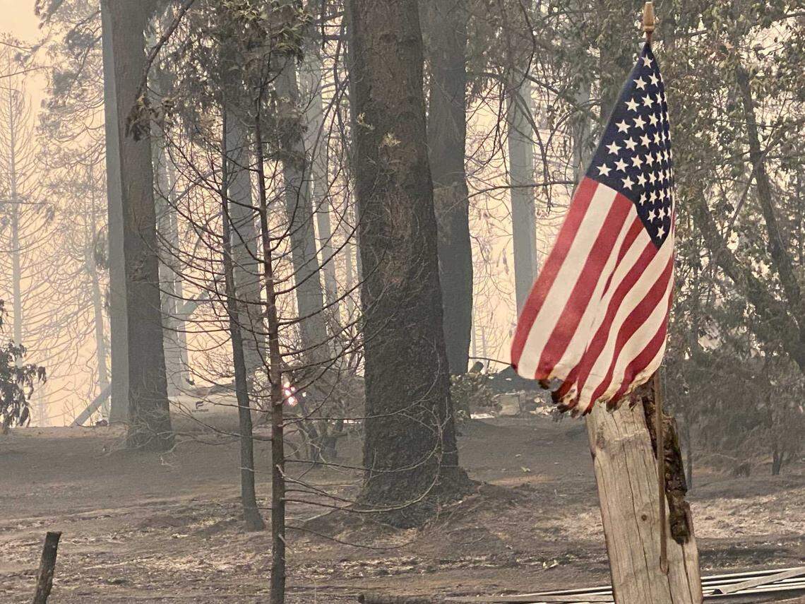An singed American flag waves in the breeze along Volcanoville Road in El Dorado County where several homes were destroyed by the Mosquito Fire, which has burned more than 25,000 acres in three days.