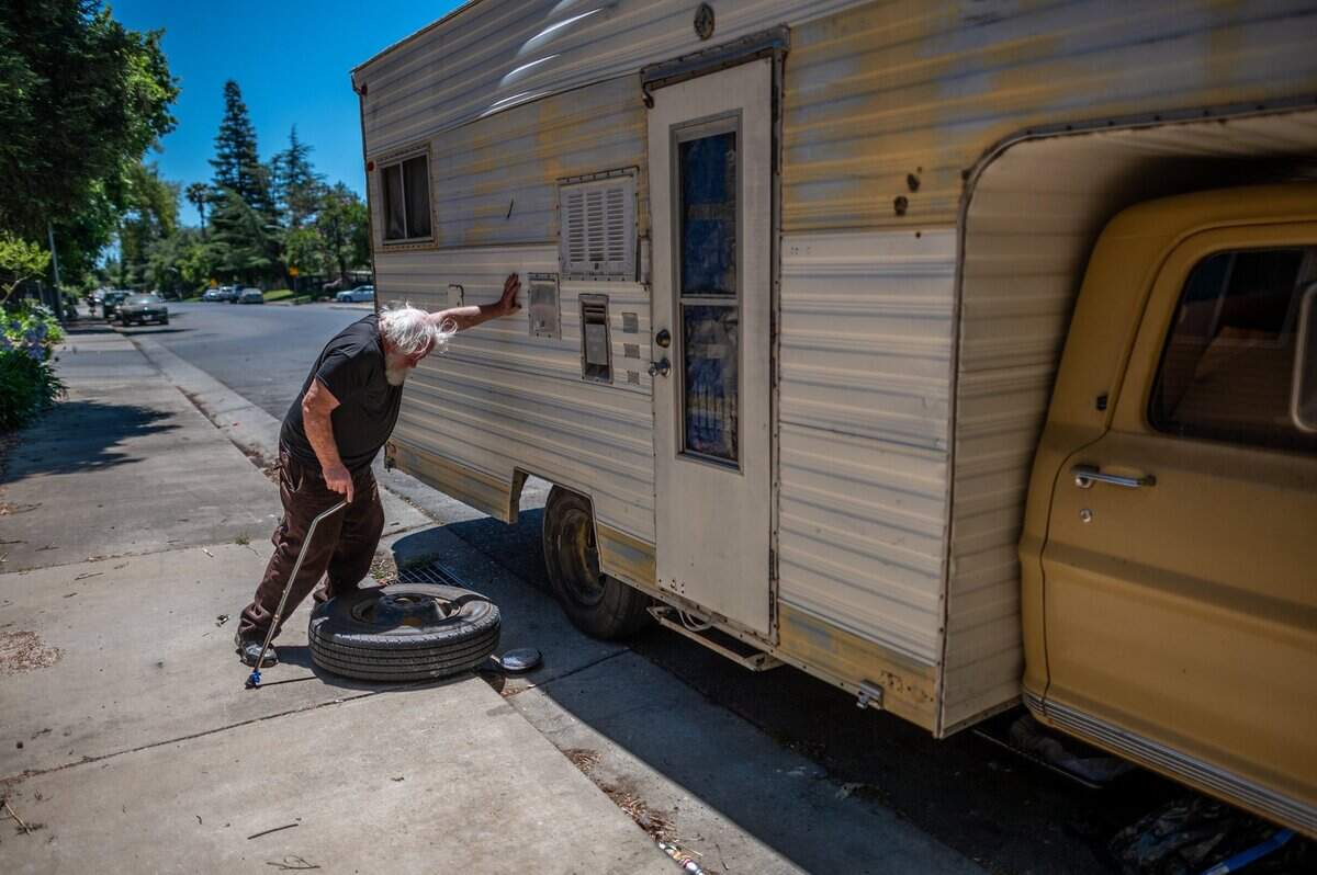 After rolling a tire down the sidewalk in hopes of finding someone to help him replace his flat tire, Donald Lowery, 73, rests against his camper he is trying to fix June 14, at the end of Hamilton Street in Sacramento. He was recently released from the hospital and says he was kicked out of the Comfort Inn and Suites in Rancho Cordova, where he had been a guest under Project Roomkey since last May.