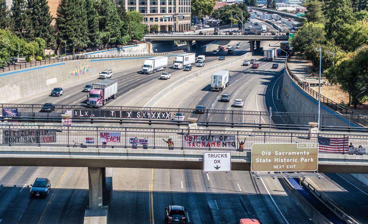 A group hangs signs in protest of President Donald Trump and his policies on the O Street overcrossing above Interstate 5 in Sacramento on Friday, Aug. 29, 2025. A series of “No Kings” protests will take place across the capital region on Saturday.