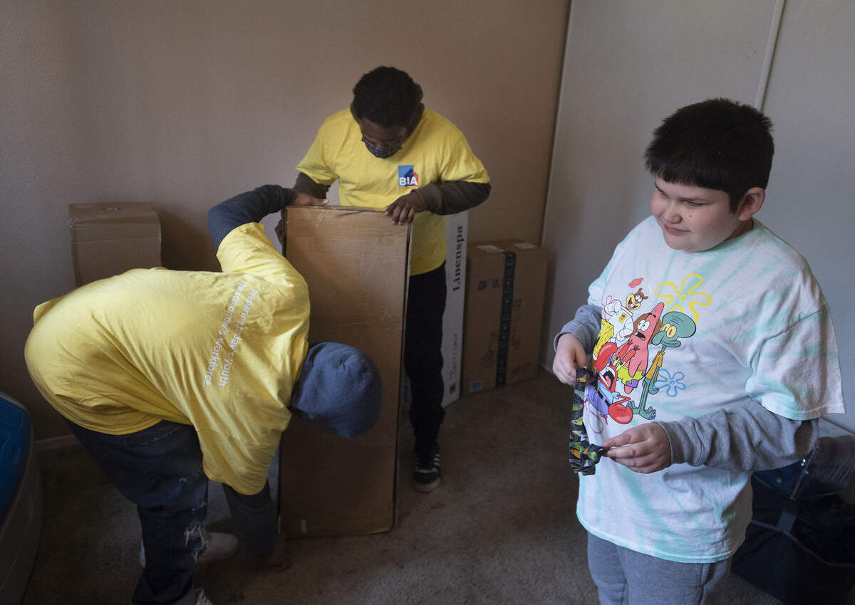 Victor Ehle Jr., 10, right, stands in his room on Monday in South Natomas while work readiness volunteers Ameir Smith, 21, left, and Jeremiah Gage, 18, assemble his new bed, provided by the North State Building Industry Foundation’s Project My Own Bed.