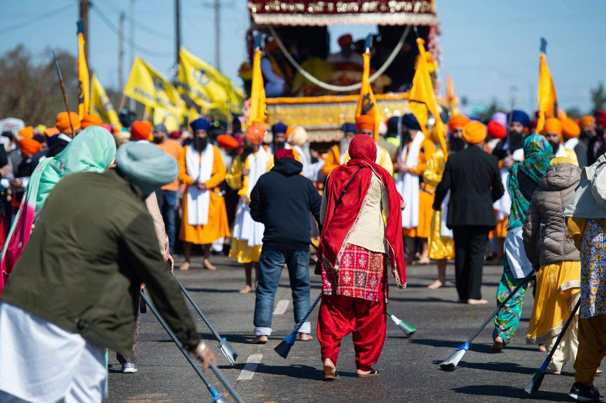 People sweep the street to clean it as a sign of respect for the float bearing the Holy Scripture during the Sacramento Sikh Society’s first Nagar Kirtan parade on Sunday, March 26, 2023, at the society’s temple in Vineyard.