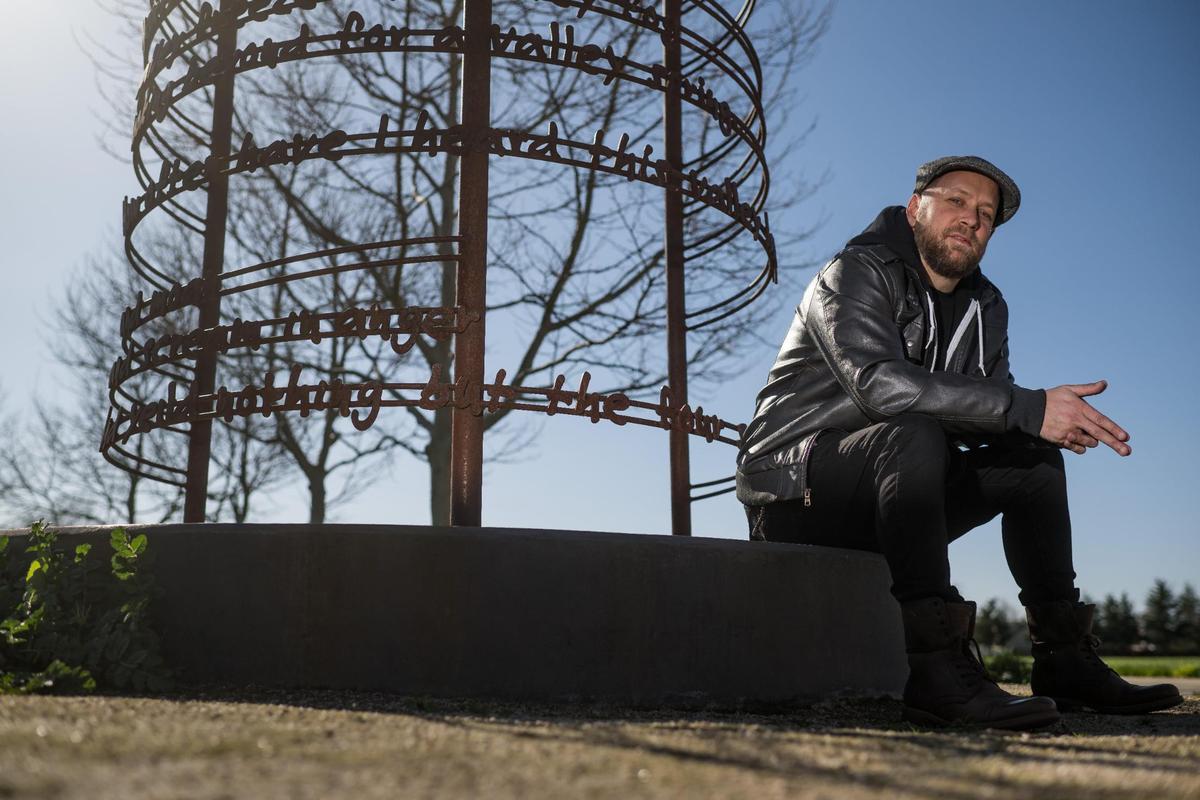 Andrew Bell, known as the the Sacramento Poet Laureate Andru Defeye, sits below a poem by José Montoya, also a former Sacramento Poet Laureate, amid regional artist Troy Corliss’ “Poet’s Path, Circle of Laureates” art installation at South Natomas Community Park on March 15.