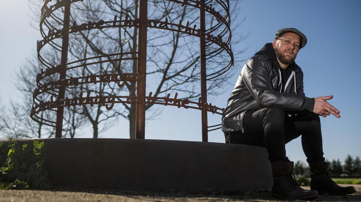 Andrew Bell, known as the the Sacramento Poet Laureate Andru Defeye, sits below a poem by José Montoya, also a former Sacramento Poet Laureate, amid regional artist Troy Corliss’ “Poet’s Path, Circle of Laureates” art installation Wednesday, March 15, 2023, at South Natomas Community Park.