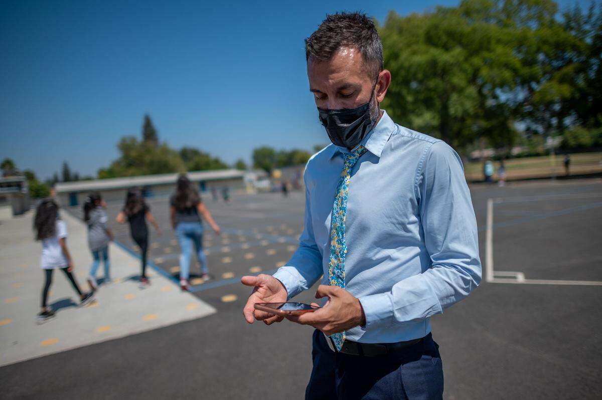 Ethel I. Baker Principal Nate McGill reads a text during recess at the school on Thursday, the first day back, while corresponding with the father of three students stranded in Afghanistan. The children and their mother spend days trying to get to the Kabul airport to escape the country and return to Sacramento, where they have lived for four years.