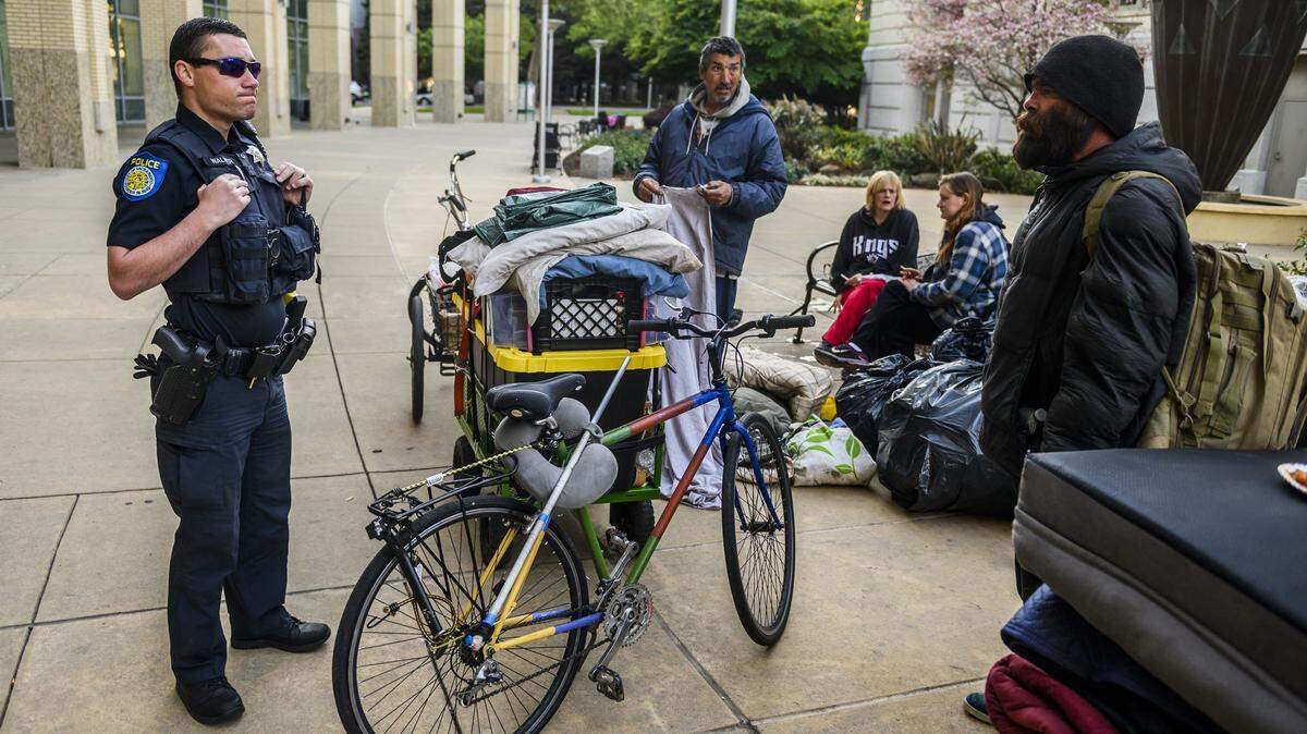 Wesley Simmons, right, a person experiencing homelessness, talks to a Sacramento Police officer after they directed campers to clean up outside of City Hall in 2020