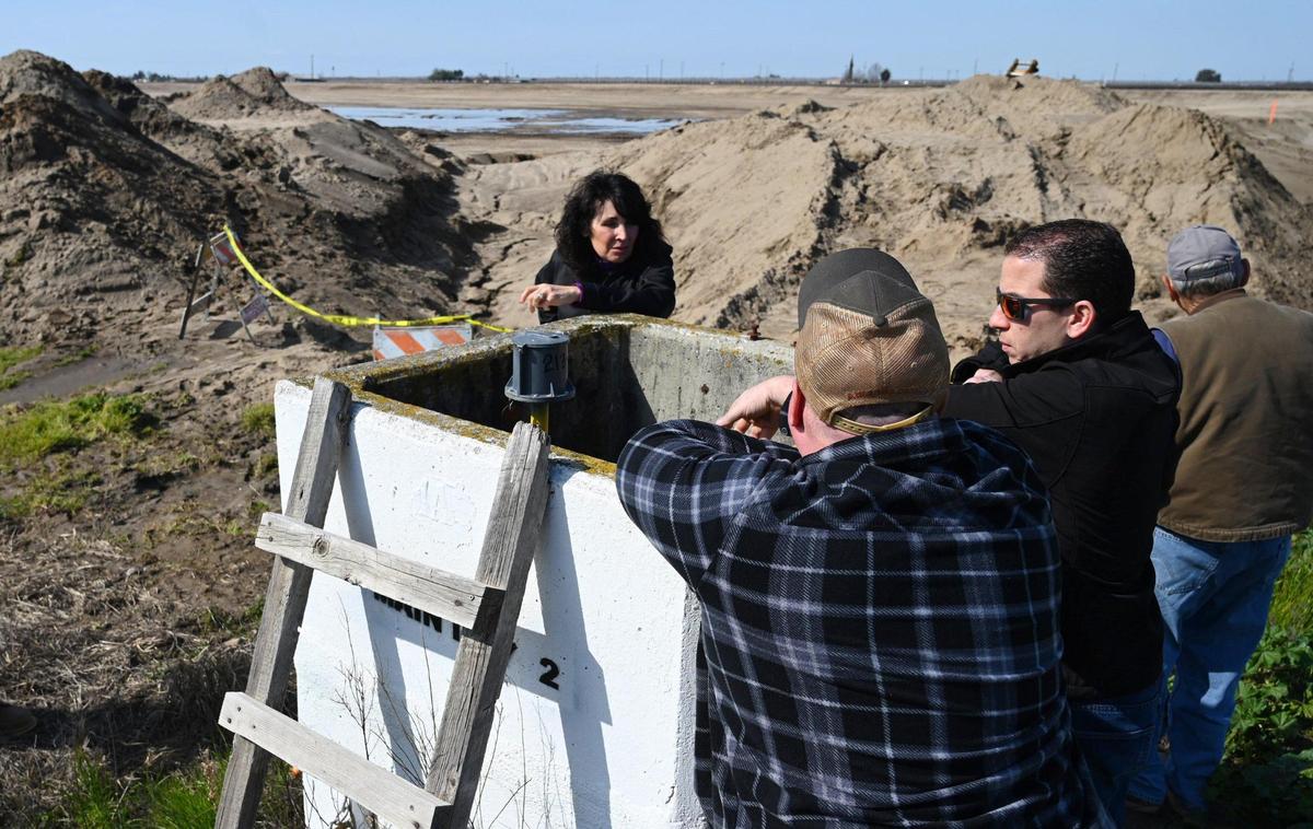 Jennifer Peters, of Markarian Family LP, center, leans on Friday against a concrete meter box while discussing with neighbors the new experimental basin to replenish groundwater at her ranch near Madera.