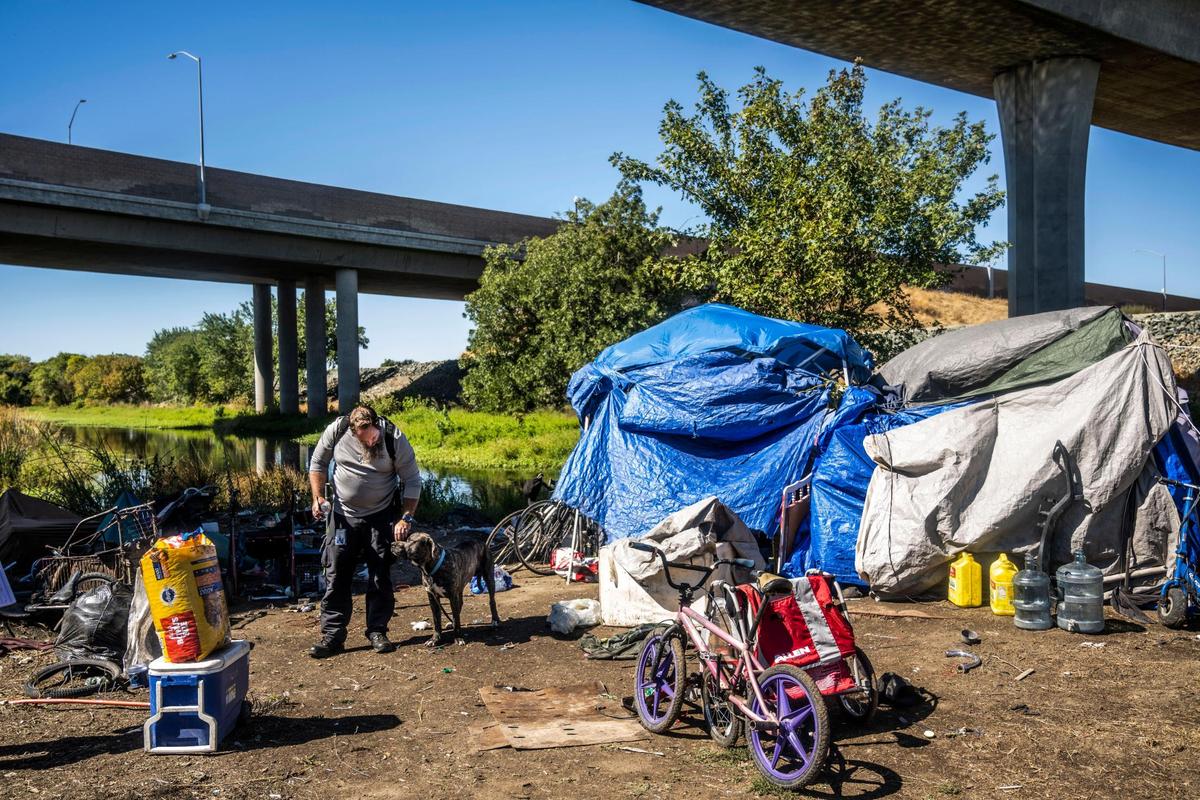 Nathan Cox, a city of Sacramento neighborhood resource coordinator, pets a dog at a homeless community of Hmong on Morrison Creek on Thursday. His department was visiting to give the community notice that it must leave the area, which is subject to flooding in the winter, in two weeks for utility cleanup.