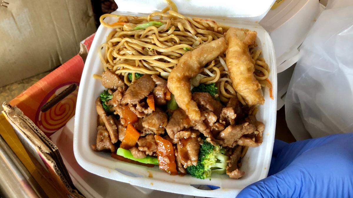 Alex Eng, president of the CACS Council, holds open a boxed lunch full of chow mein, beef with broccoli and fried chicken.