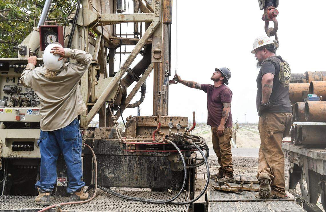 John Hicks, left, Terry Hicks, center, and Jason Tate of Strickland Drilling operate a drilling rig during a groundwater drilling operation in a walnut orchard near Caruthers in the central San Joaquin Valley earlier this month.