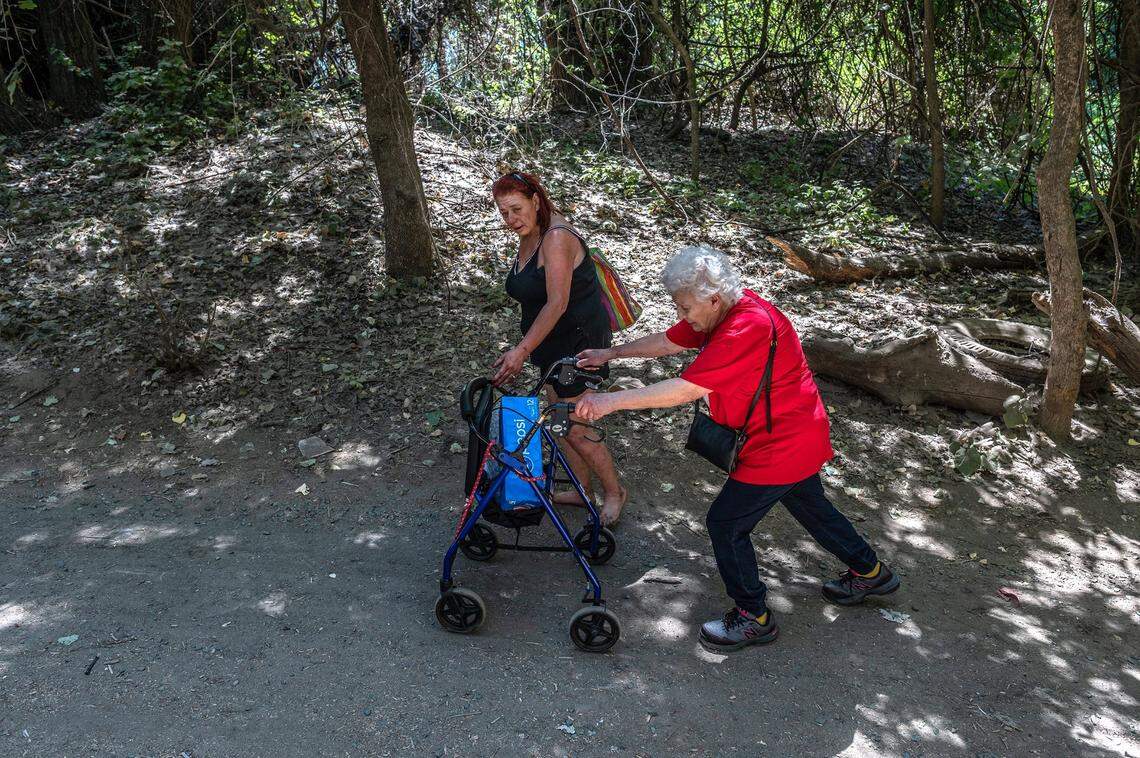 Twana James walks with Patricia Berry, 72, as she makes her way with a walker to visit the residents of “the island” in July, after she got into housing.