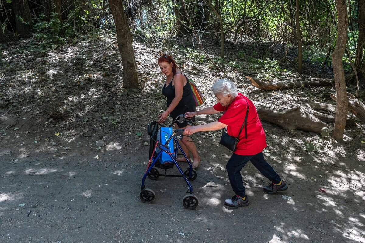 Twana James walks with Patricia Berry, 72, as she makes her way with a walker to visit the residents of “the island” in July, after she got into housing.
