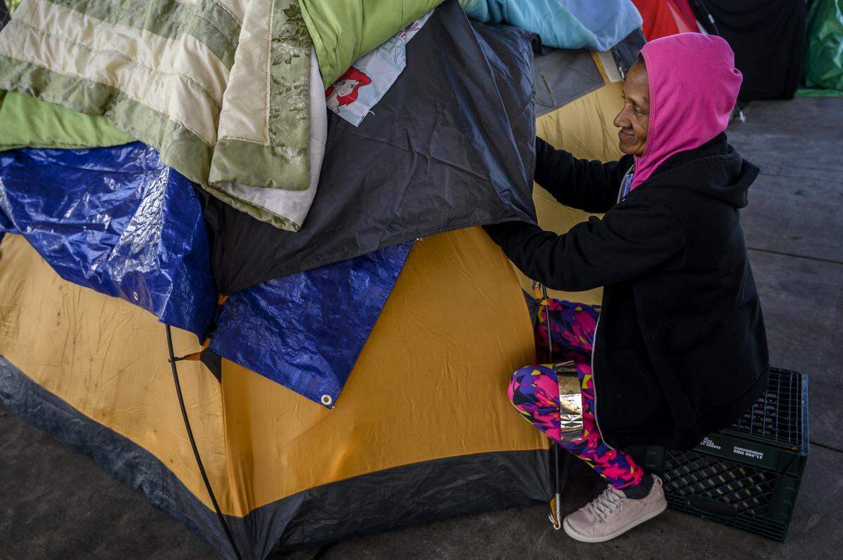 Lois Caesar, 57, tapes her tent while preparing for another night sleeping outdoors in near-freezing temperatures on Thursday, Jan. 2, 2020, on X Street in Sacramento. Her tent is one of about 15 that lines X Street, just outside a recently paved lot where the city plans to open a 100-bed shelter in May. If Caesar is still homeless when the shelter opens, she will try to get in, seeking safety, warmth, and regular meals, which she needs to cope with her diabetes.