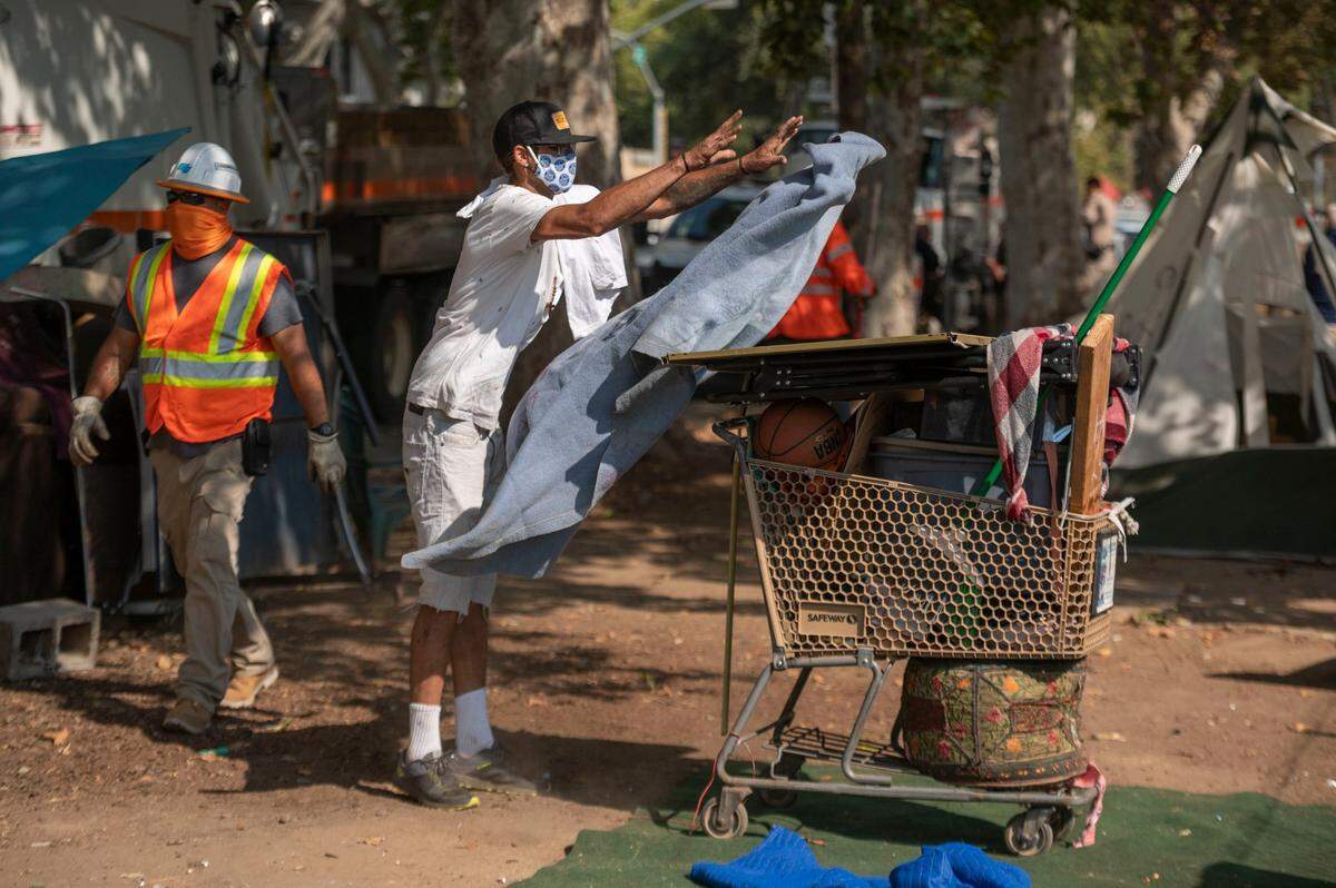 Homeless resident Naylee covers a mirror and other belongings as his camp is removed by Caltrans at 29th and G streets in Midtown Sacramento in October 2021. The agency wants more than $5 million to help clear more encampments around the state.