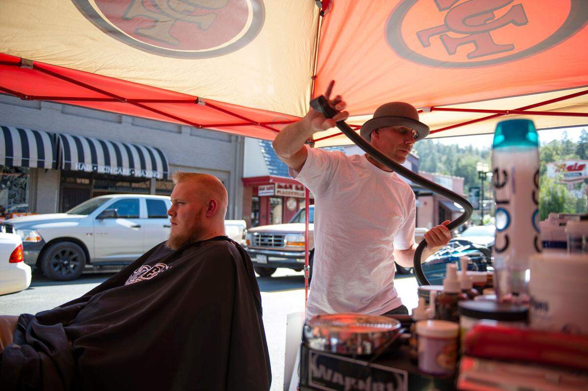 “Bowtie Barber,” the owner of Bowtie Barber Shop in Placerville, gives resident Justin Gargiulo a hair cut on the street Wednesday, Oct. 9, 2019. Barber had to drive to Sacramento to find the nearest generator for sale in the morning to open up his business during the PG&E blackouts.