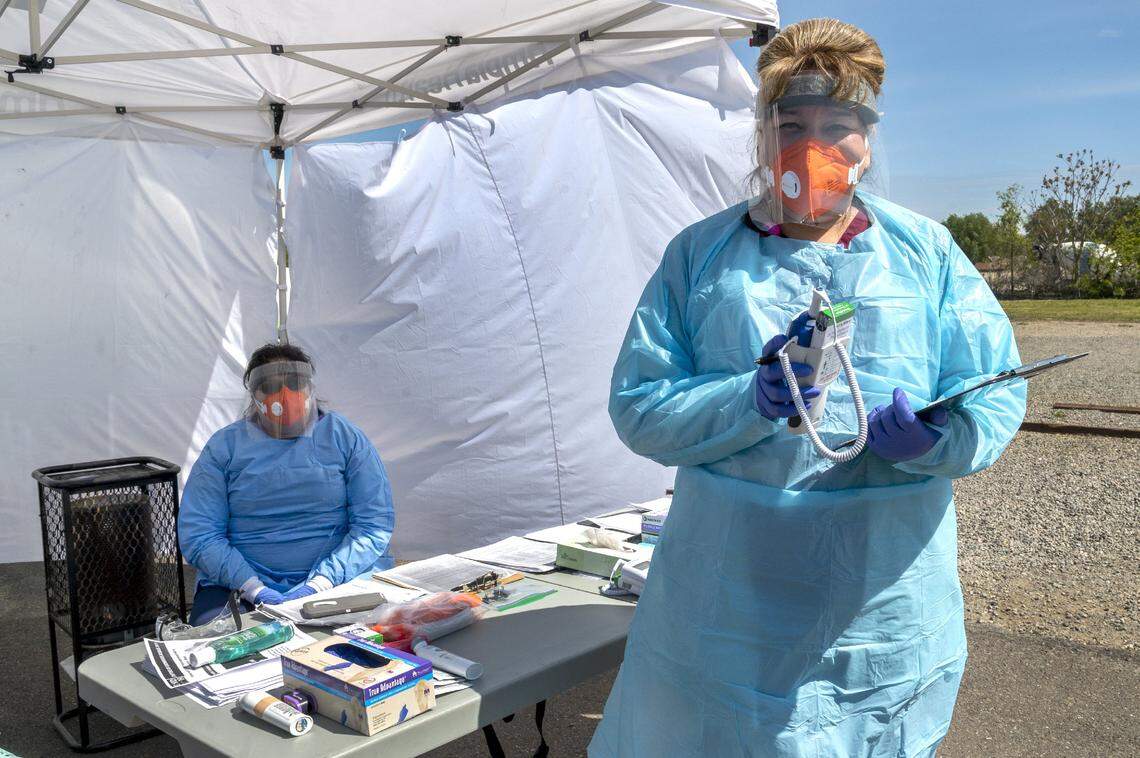 Certified nursing assistant Christy Mewborn, right, greets patients with a thermometer as part of the screening process to see if patients qualify for a COVID-19 test.