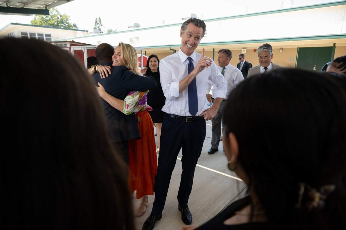 California First Partner Jennifer Siebel Newsom hugs state Superintendent of Public Instruction Tony Thurmond as Gov. Gavin Newsom talks with students at River City High School in West Sacramento on Thursday.