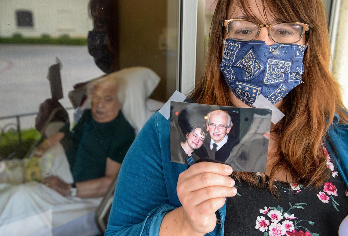Denise Plank poses with a photo of her and her father, Ed, 84, while visiting him through his nursing home window at the California Armenian Home in Fresno on Friday, April 17, 2020. Ed is suffering from a blood disease but Denise continues to visit him nearly every day, if only through his nursing home window.