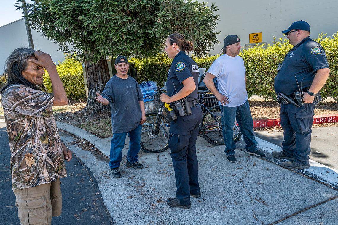Homeless outreach officers Jennifer McCue, left, and Chris Cahill of the Elk Grove Police Department, talk to unhoused residents on July 19 who lost their belongings after a fire broke out at their encampment underneath a pedestrian bridge spanning Highway 99 north of Elk Grove Boulevard. A new Elk Grove ordinance is clamping down on homeless campers. It bars the city’s unhoused from camping within 500 feet of daycare centers, schools, playgrounds or youth centers; bans encampments without permitted electric, water and sewage hookups; and prohibits camping on private property without the property owners permission