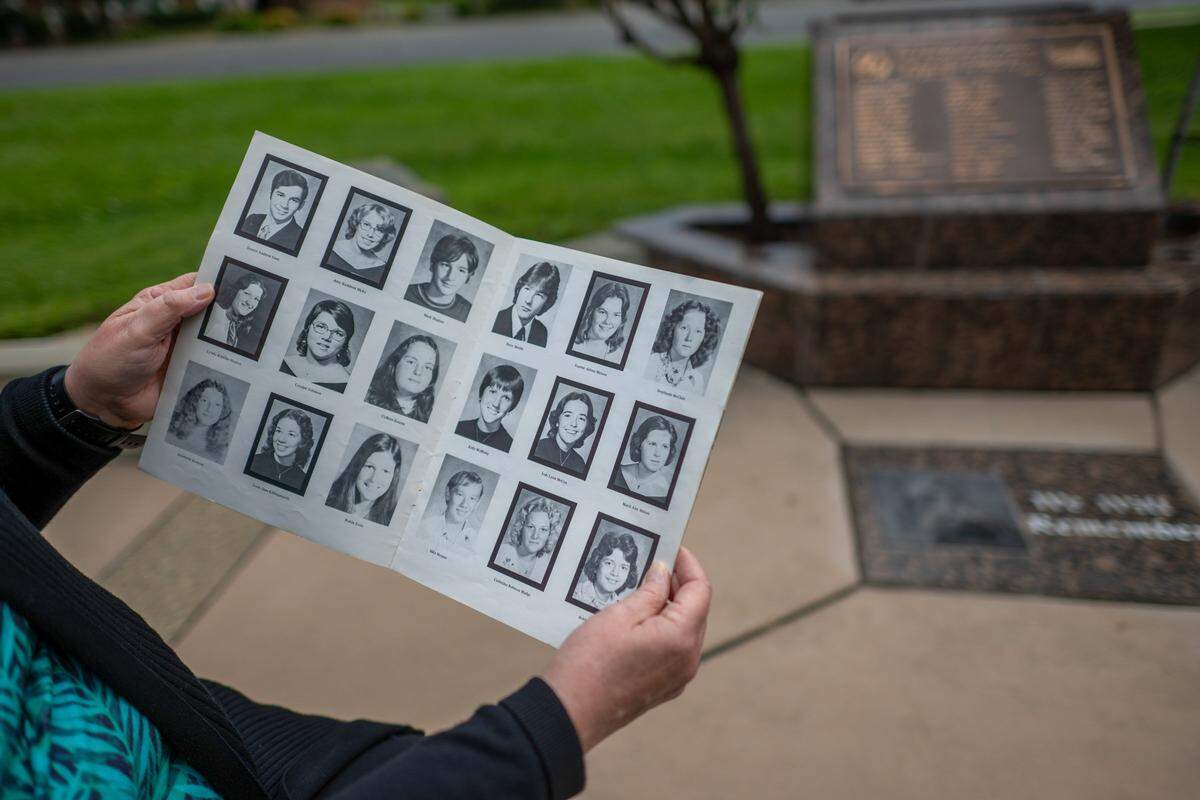 Donna Peacock Sorenson, a survivor of the bus crash that killed 28 members of the Yuba City High School A Cappella Choir and a teacher, holds a yearbook supplement showing portraits framed in black for those who were killed and unframed portraits for survivors as she stands beside a memorial site in Yuba City Monday, May 4, 2026. The special section spans several pages representing those who lost their lives and those who survived the May 21, 1976, tragedy.